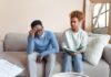 Couple sitting on a couch having a tense conversation while working through relationship anxiety
