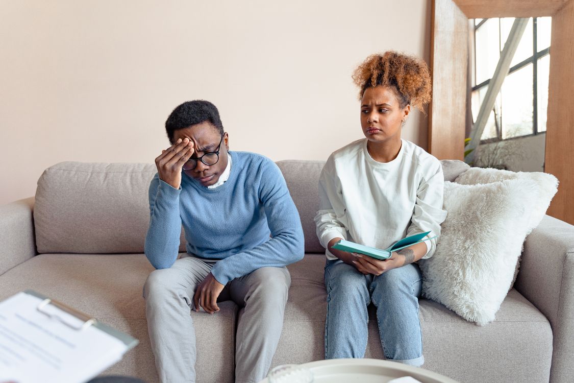 Couple sitting on a couch having a tense conversation while working through relationship anxiety