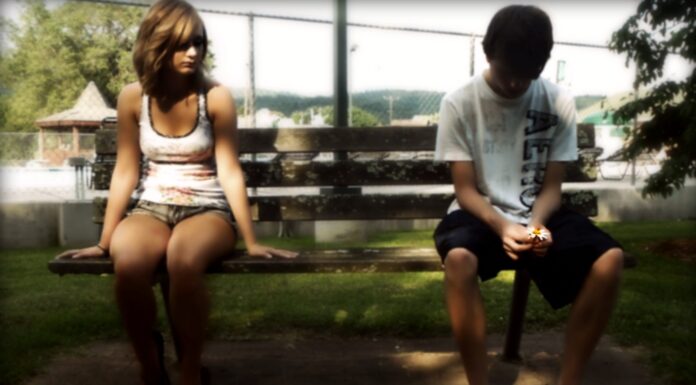 Young couple sitting apart on a park bench, illustrating emotional distance and silence in a relationship