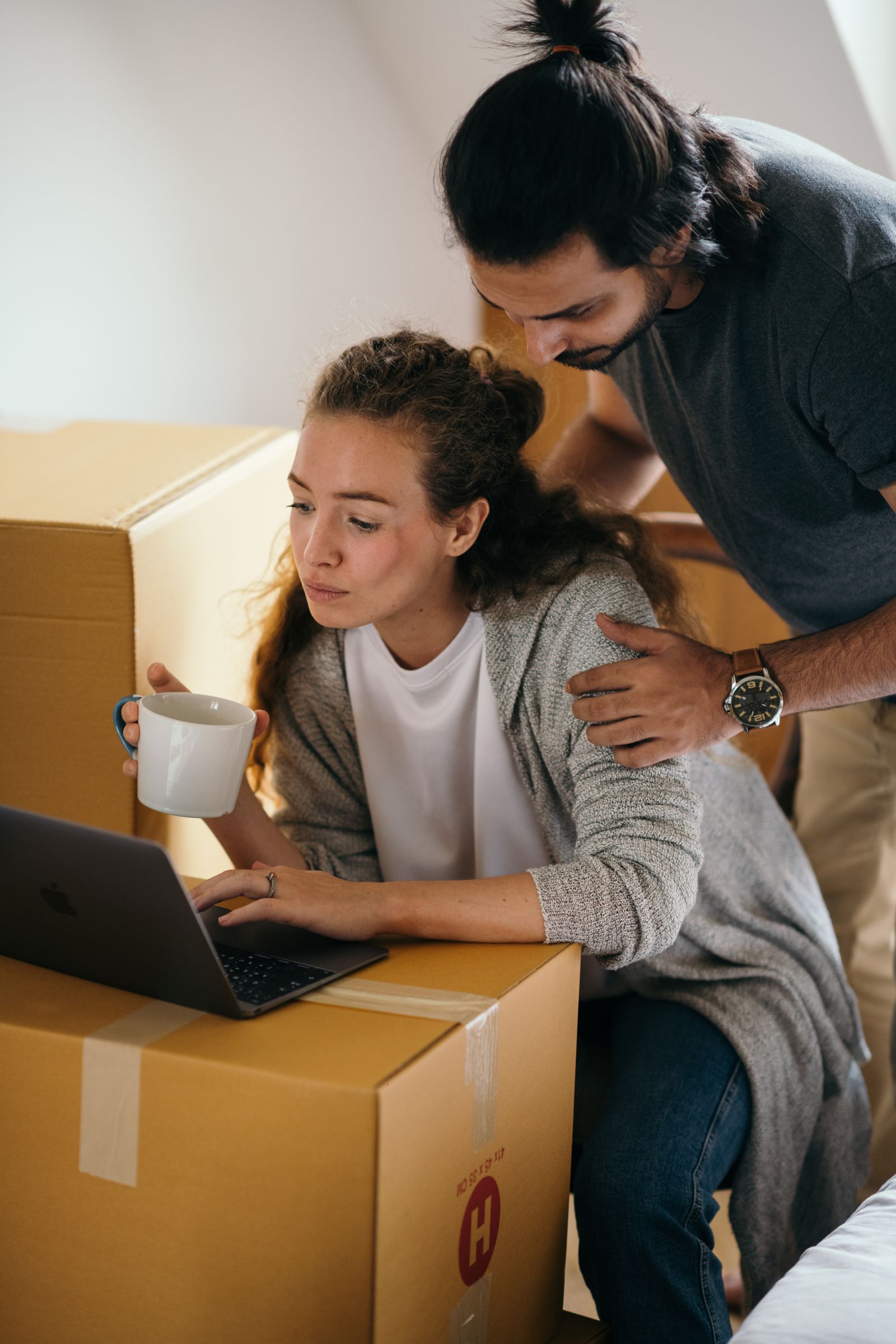 Couple researching a possible move on a laptop beside packed boxes
