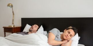 One partner lying awake in bed while the other sleeps and snores