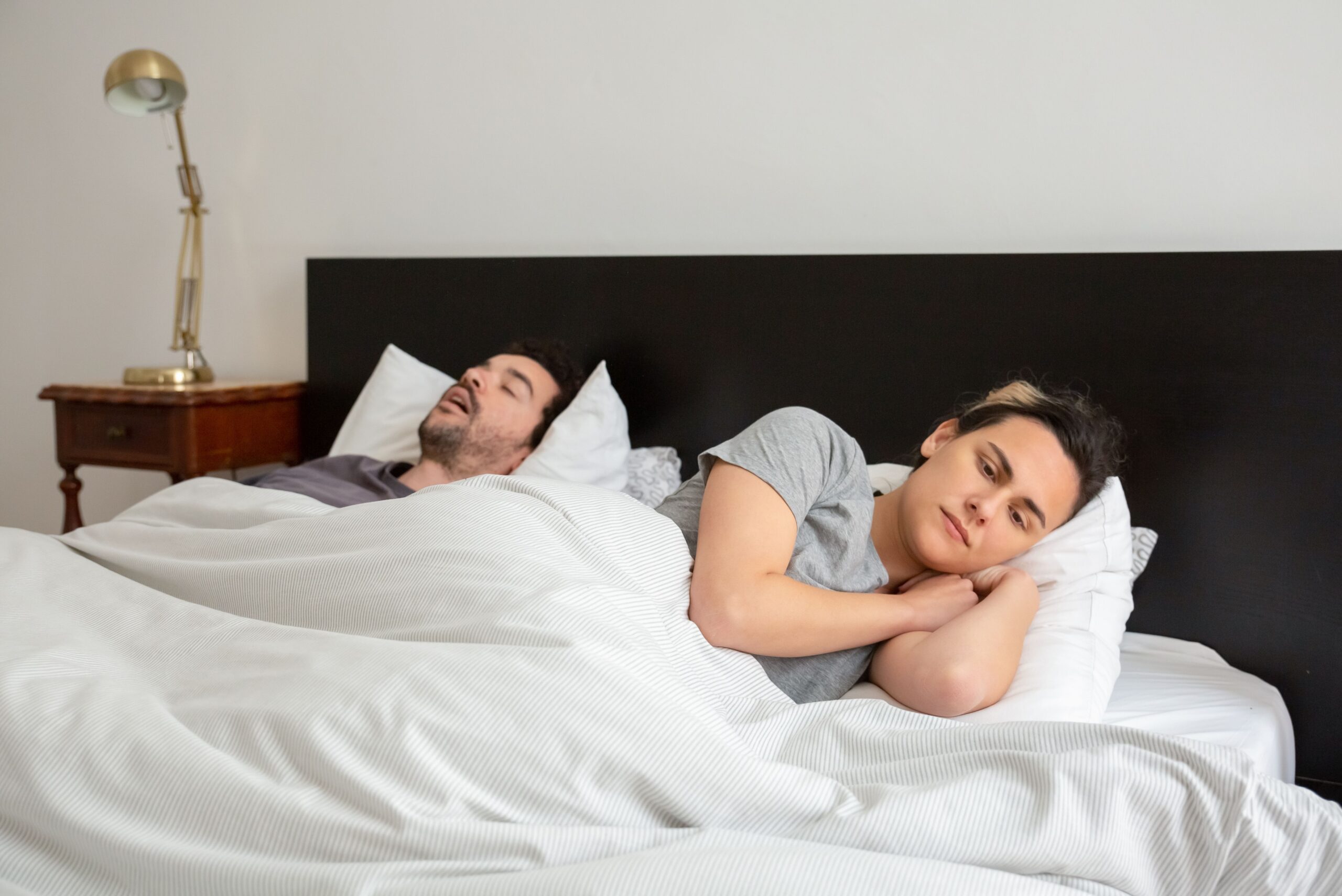 One partner lying awake in bed while the other sleeps and snores