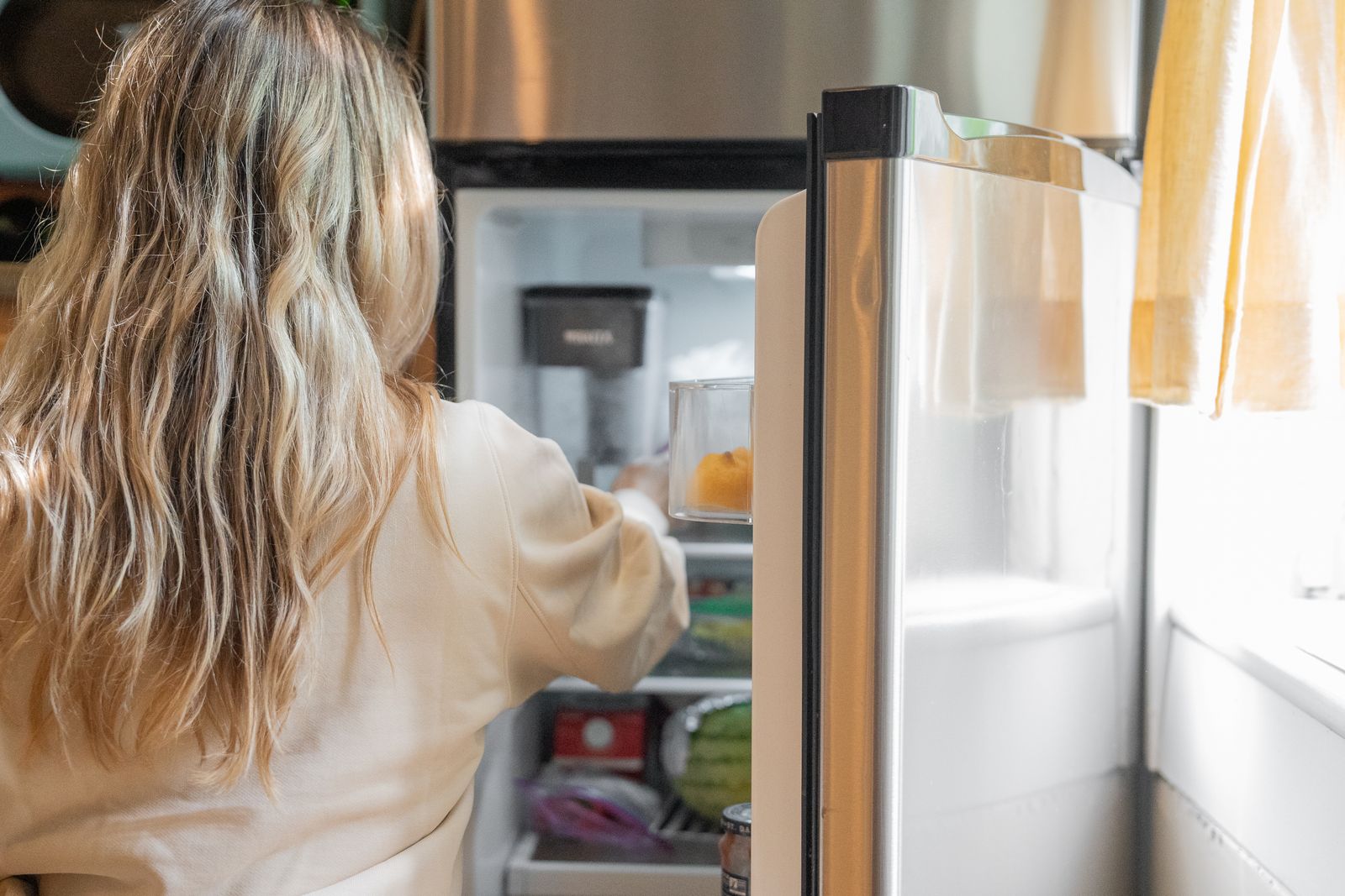 Person checking food containers and groceries in an open refrigerator