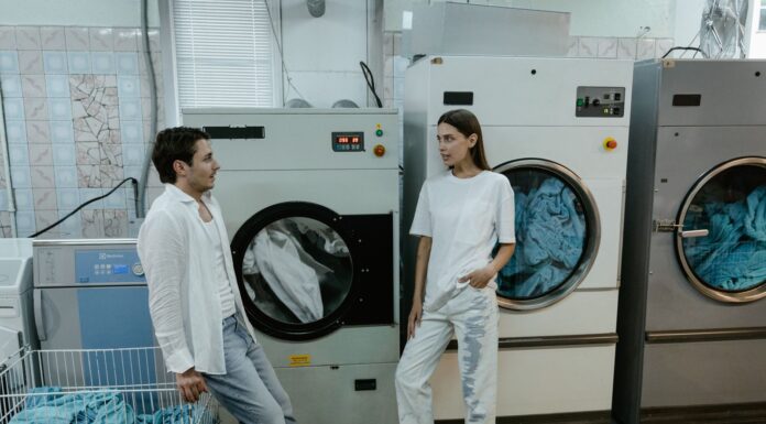 When Your Partner Never Cleans the Dryer Lint Trap: How to Share Laundry Safety Without Nagging Couple discussing laundry responsibilities beside washing machines