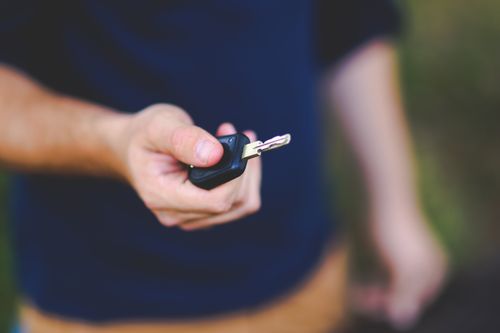 Hand holding a car key beside a vehicle after confirming the doors are locked