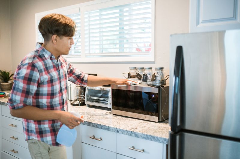 Man cleaning a microwave in a home kitchen with a cloth