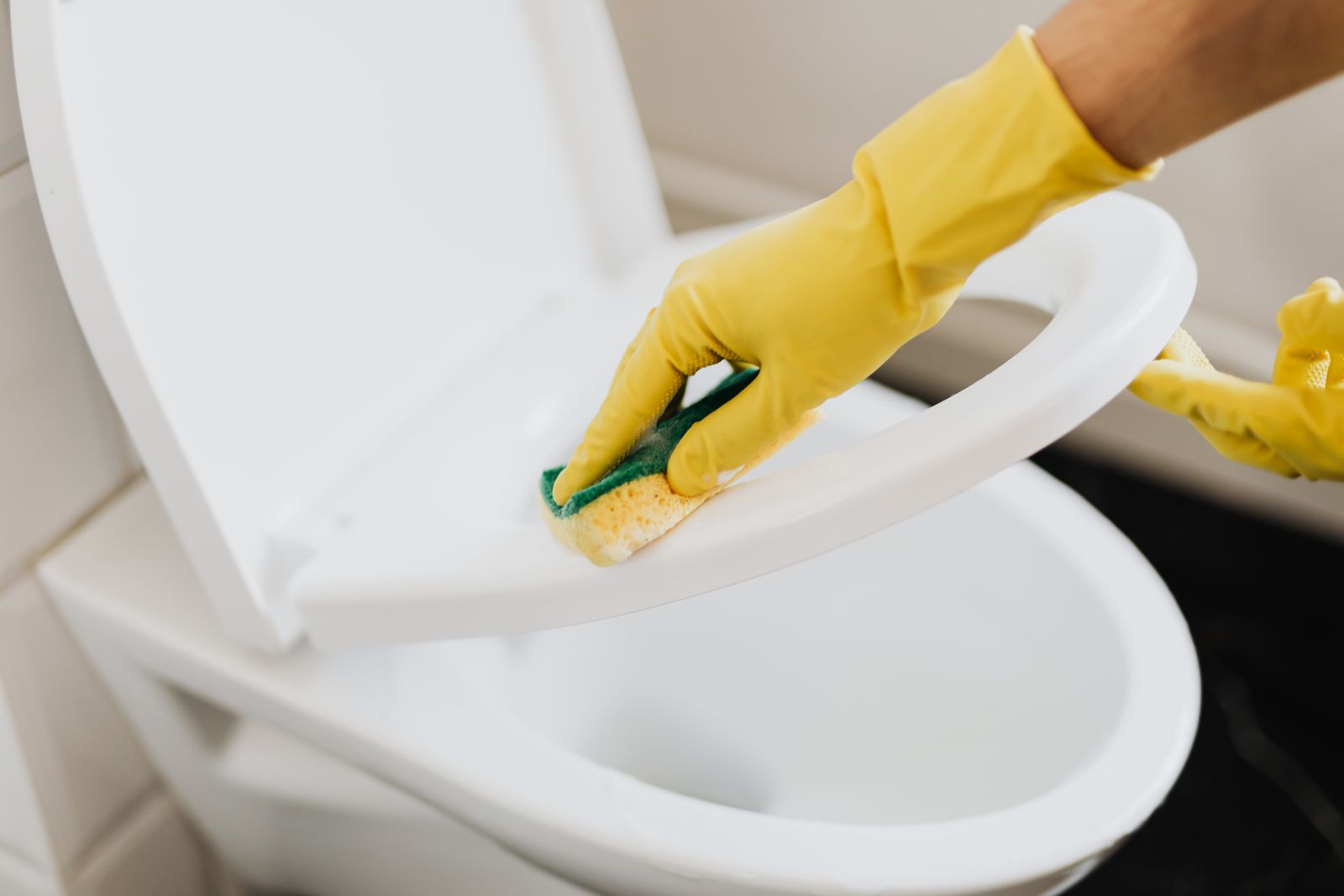 Person wearing gloves while cleaning a toilet seat