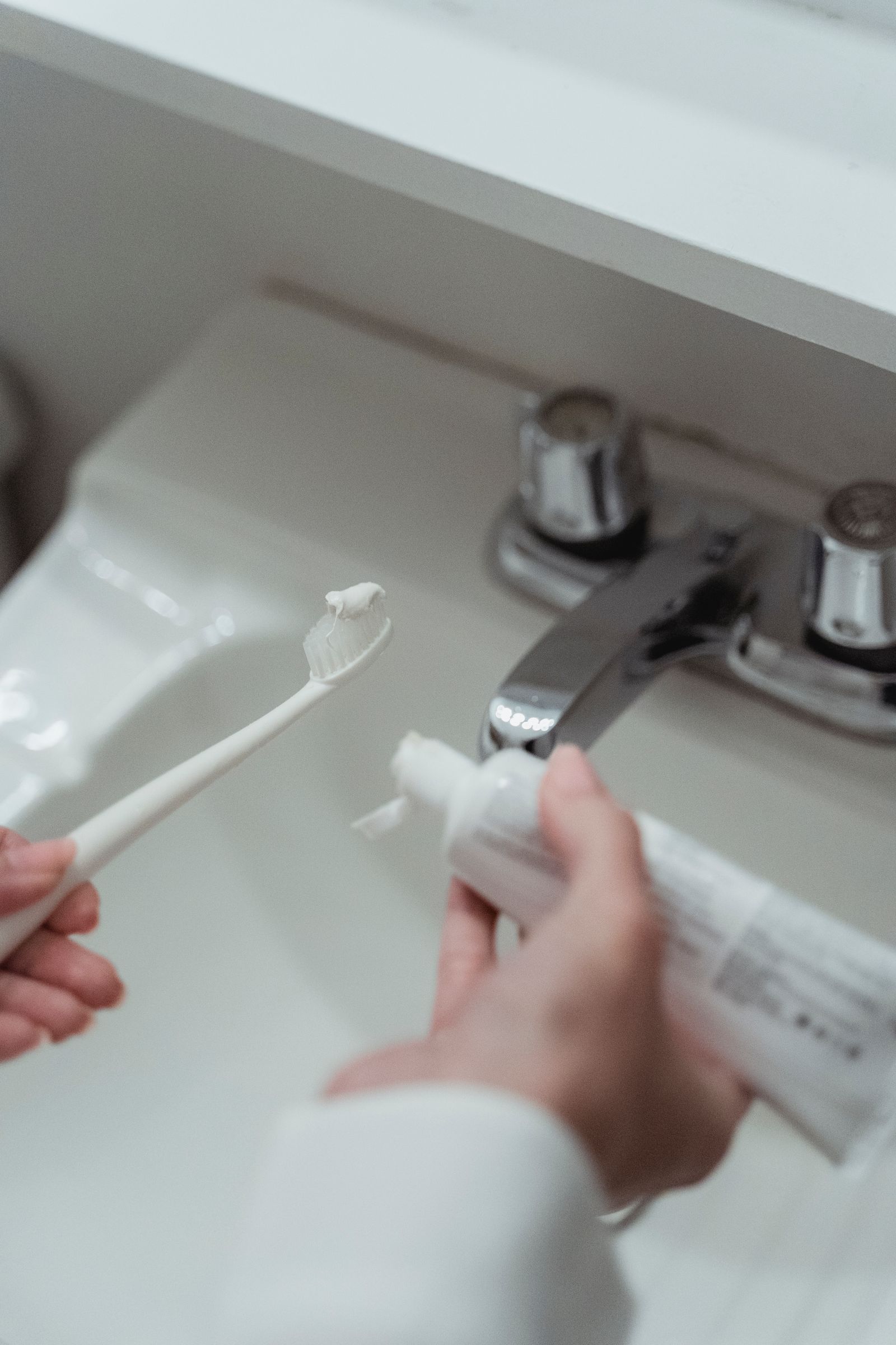 Person applying toothpaste to a toothbrush over a bathroom sink