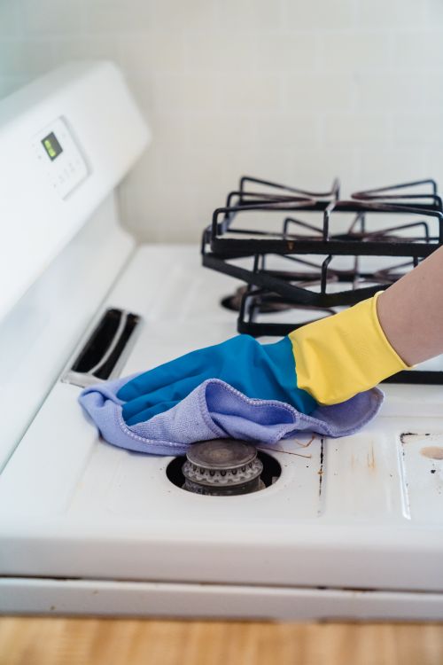 Gloved hand wiping grease from a gas stovetop after cooking