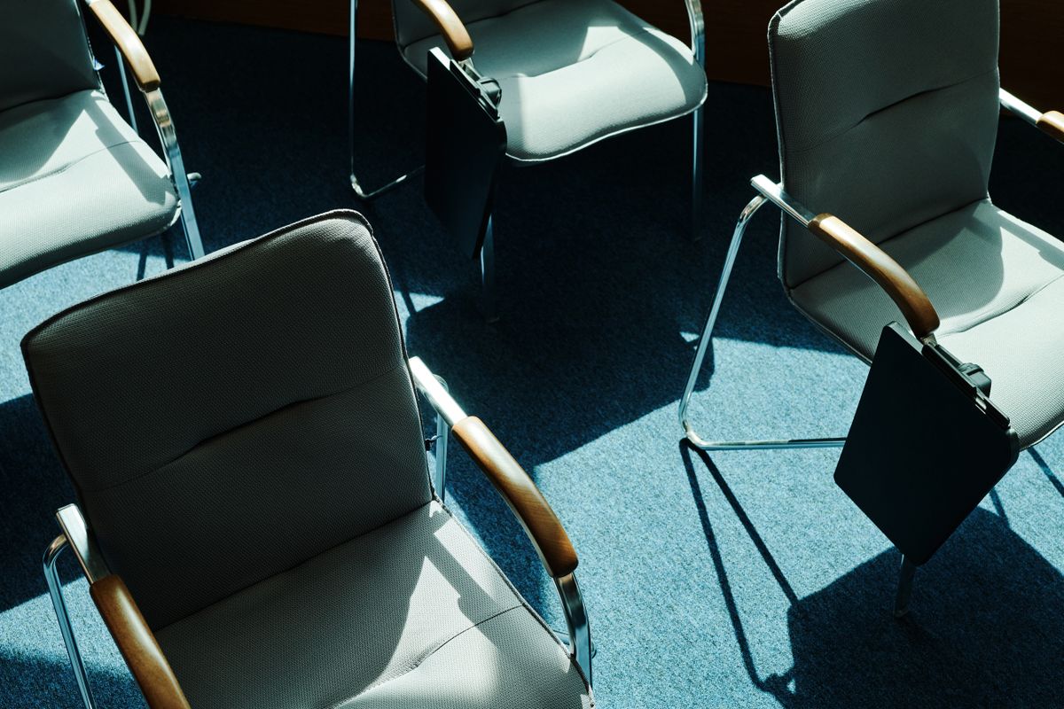 Empty metal-framed chairs casting shadows across a sunlit meeting room