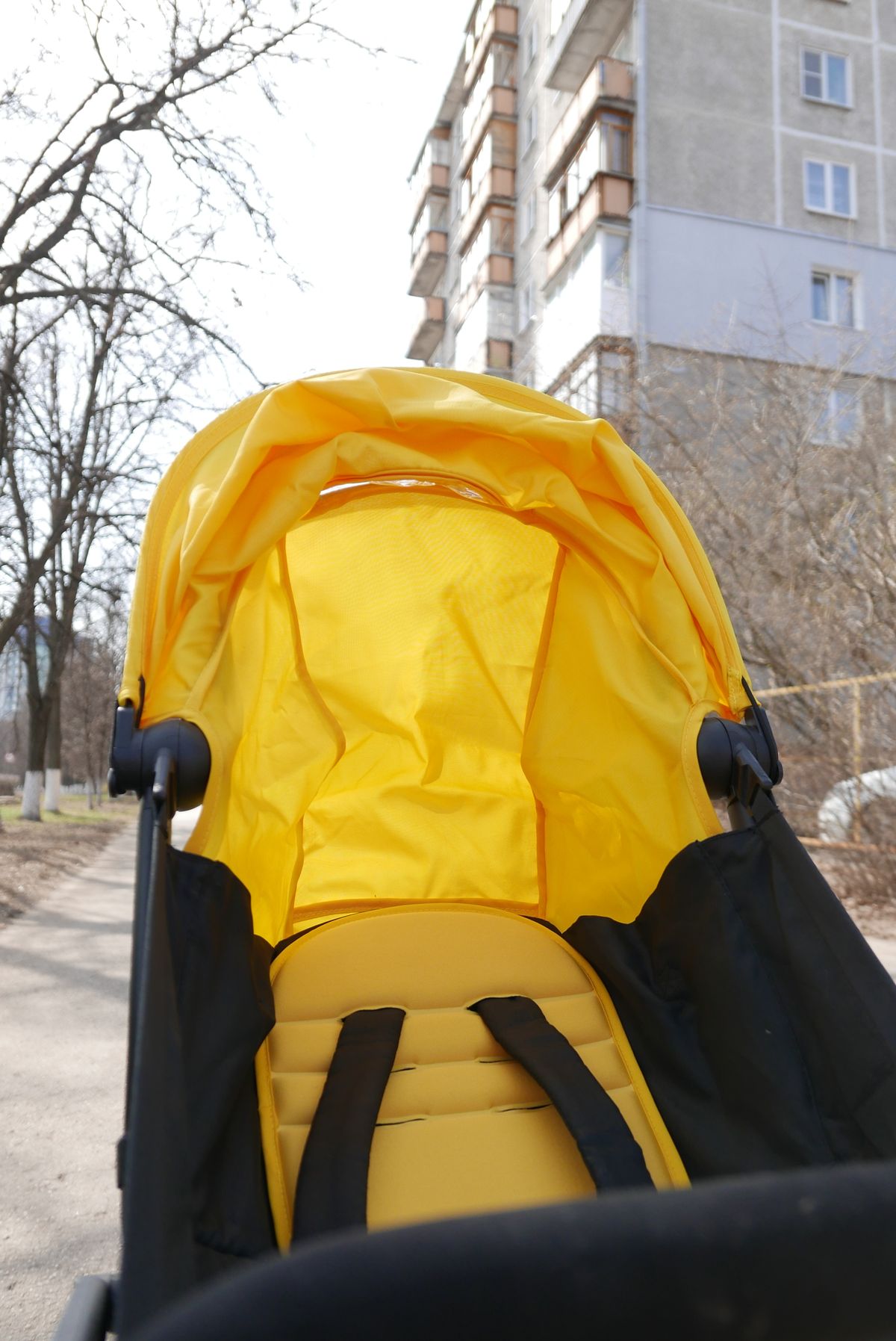 Yellow baby stroller standing in sunlight on a city sidewalk