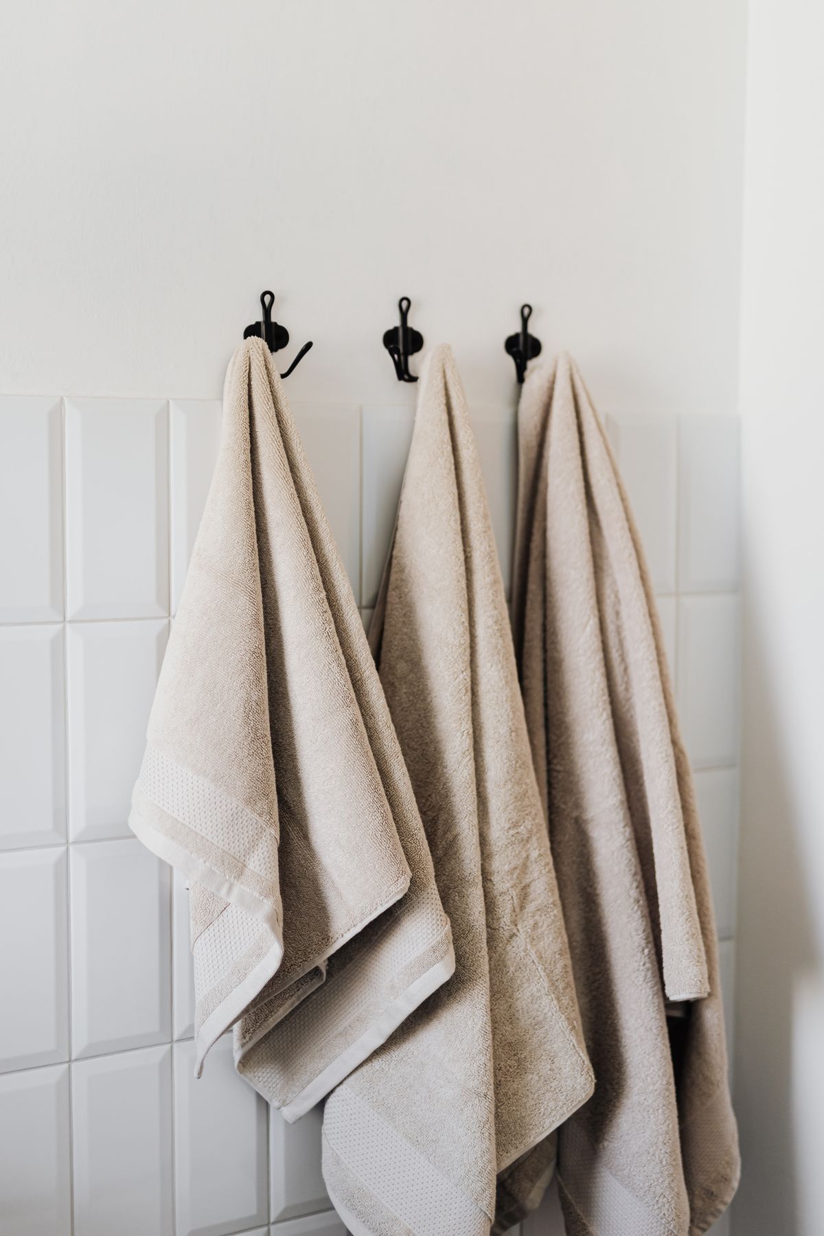 Beige household towels hanging separately on bathroom hooks to dry