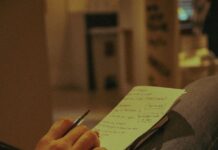 Person holding a pen and writing on paper indoors