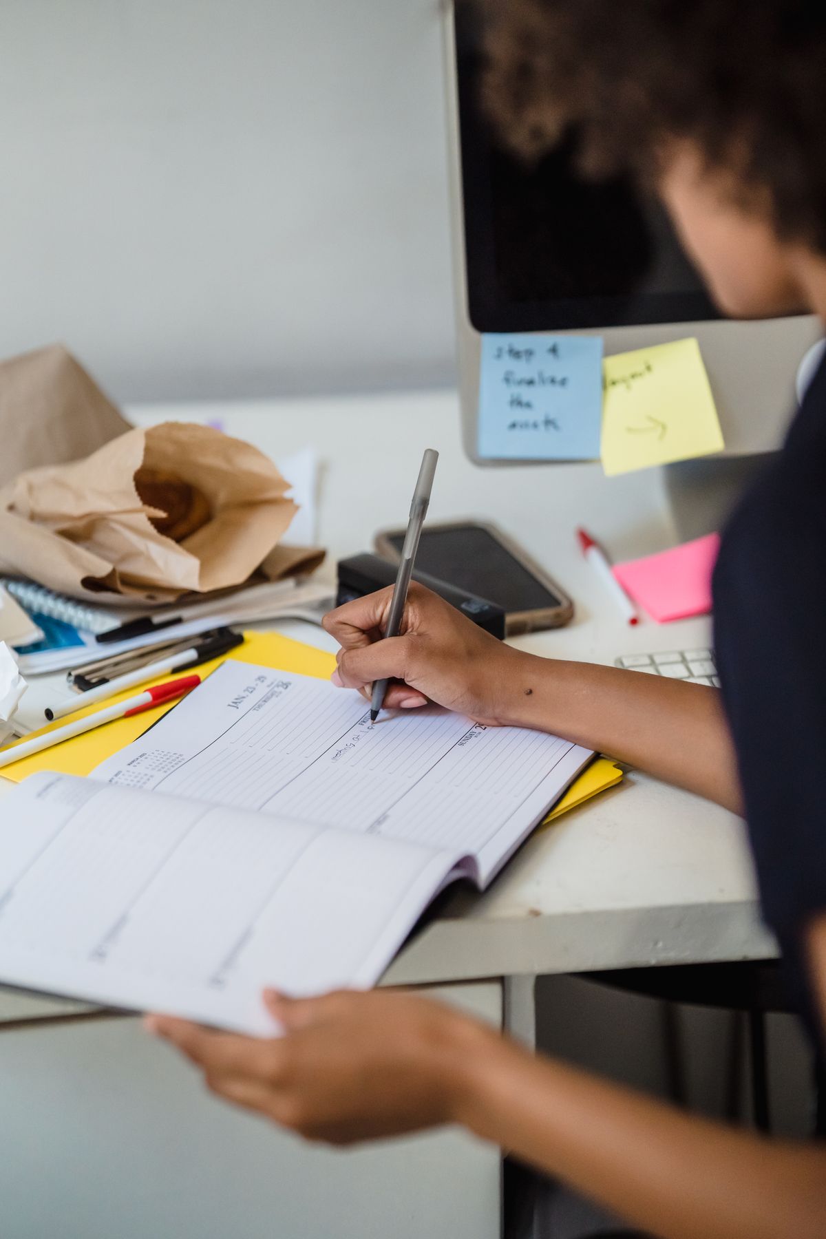 Person writing in a paper planner at an office desk