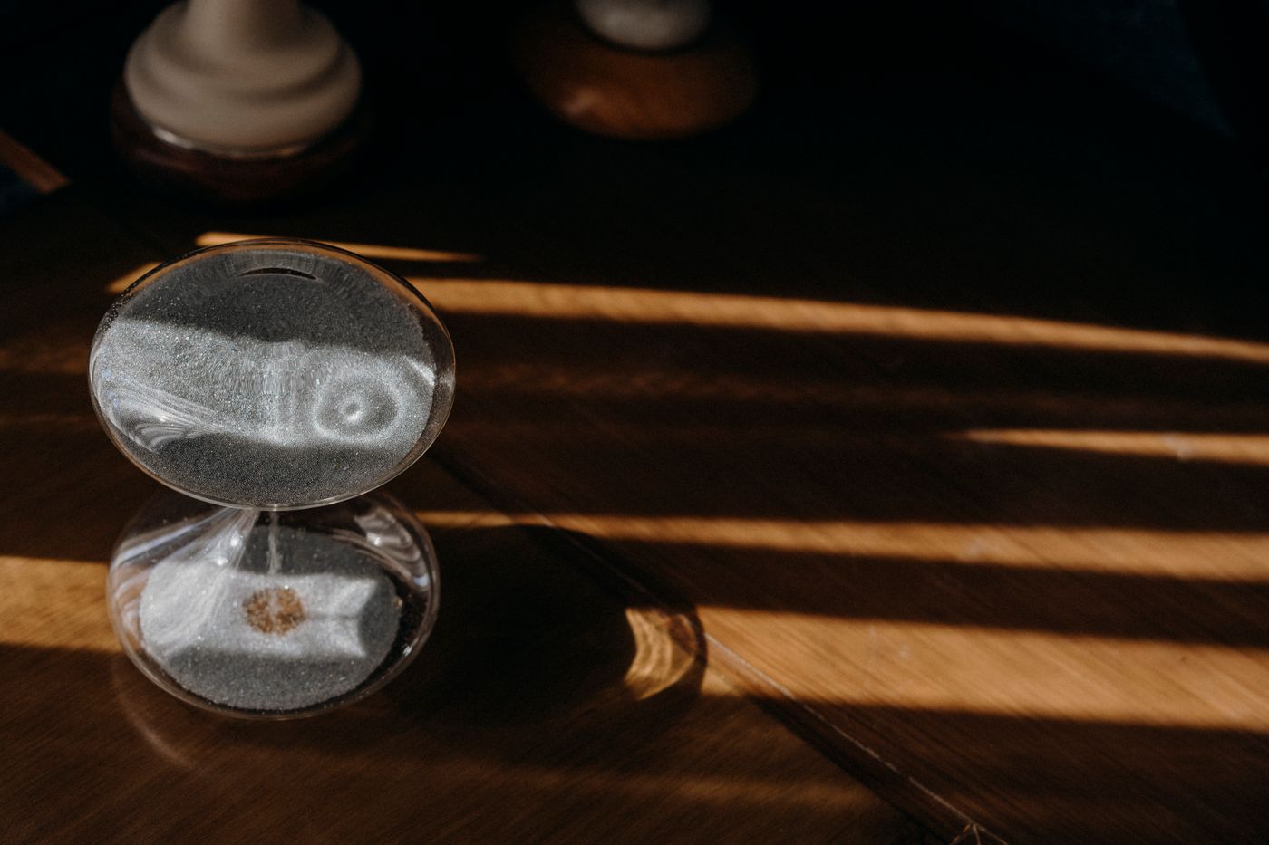 Glass sand timer casting a shadow on a wooden table in sunlight