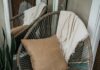 Rattan chair with a cushion and throw beside books and a plant