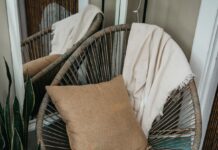 Rattan chair with a cushion and throw beside books and a plant