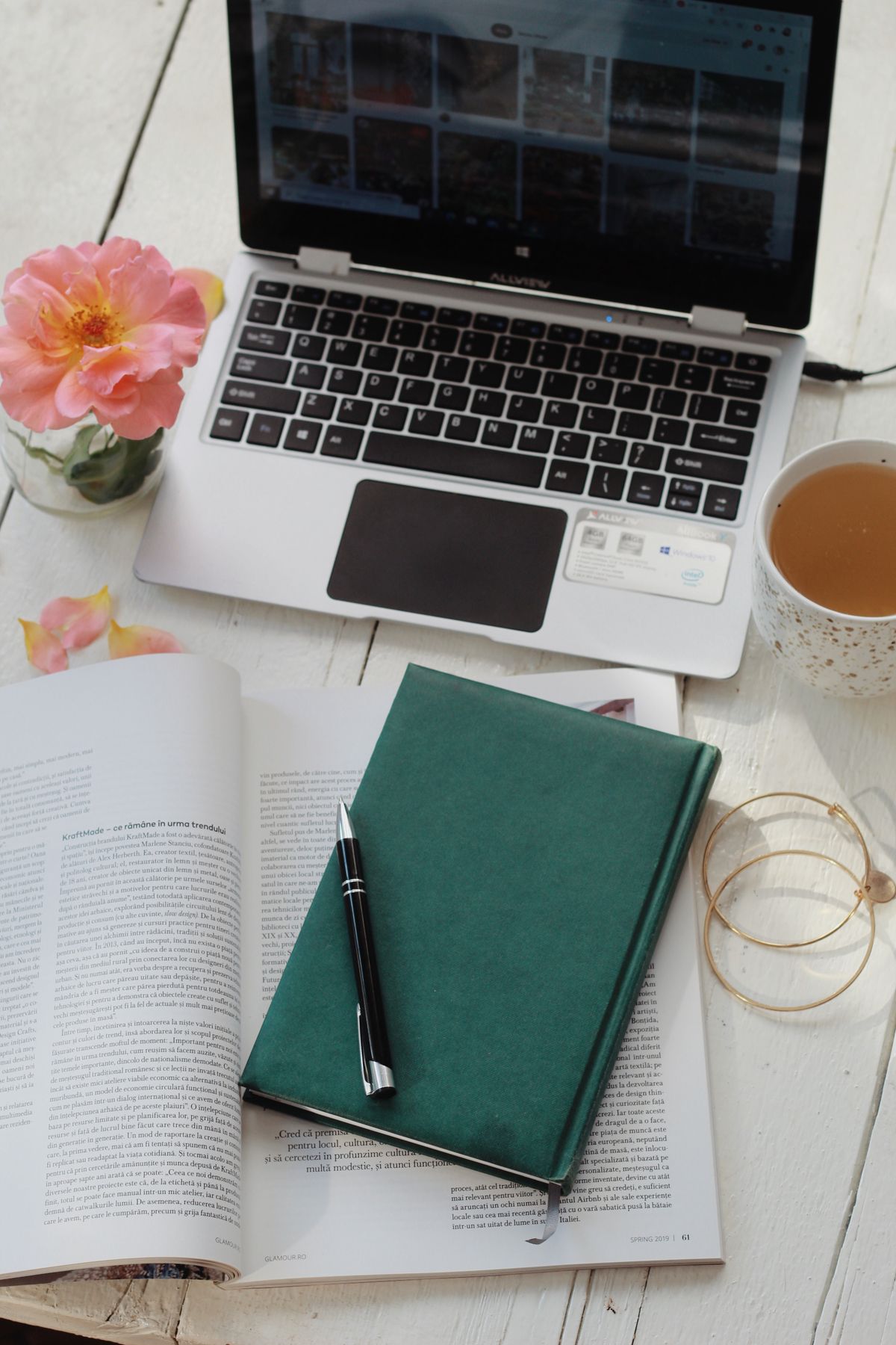 Laptop, notebook, open book, and a cup of tea arranged on a table