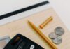 Calculator with cash and coins beside a yellow notepad and pen