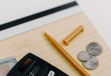 Calculator with cash and coins beside a yellow notepad and pen
