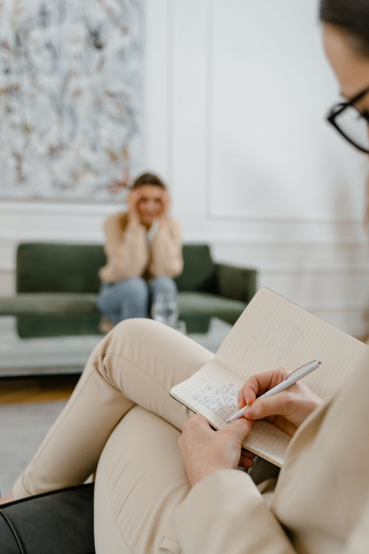 Person in beige trousers writing notes in a notebook during a conversation