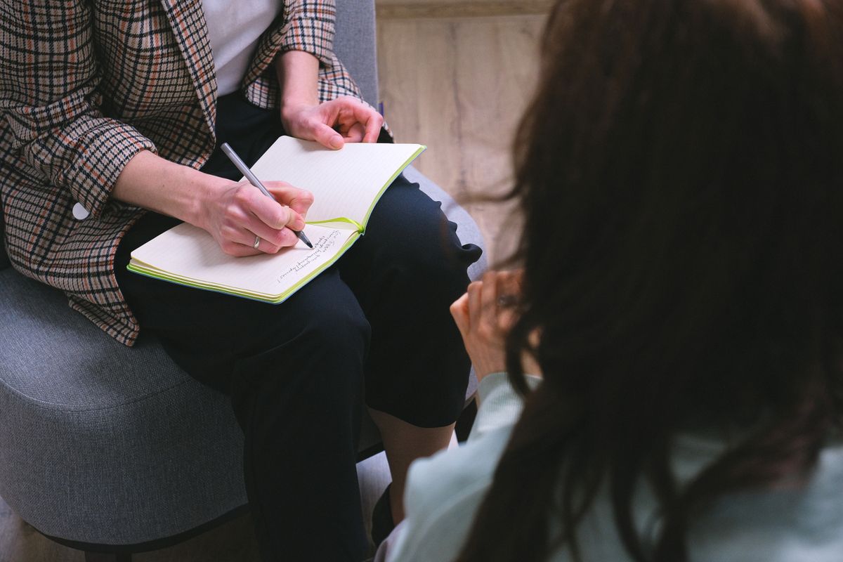 Counselor writing in a notebook while speaking with another person