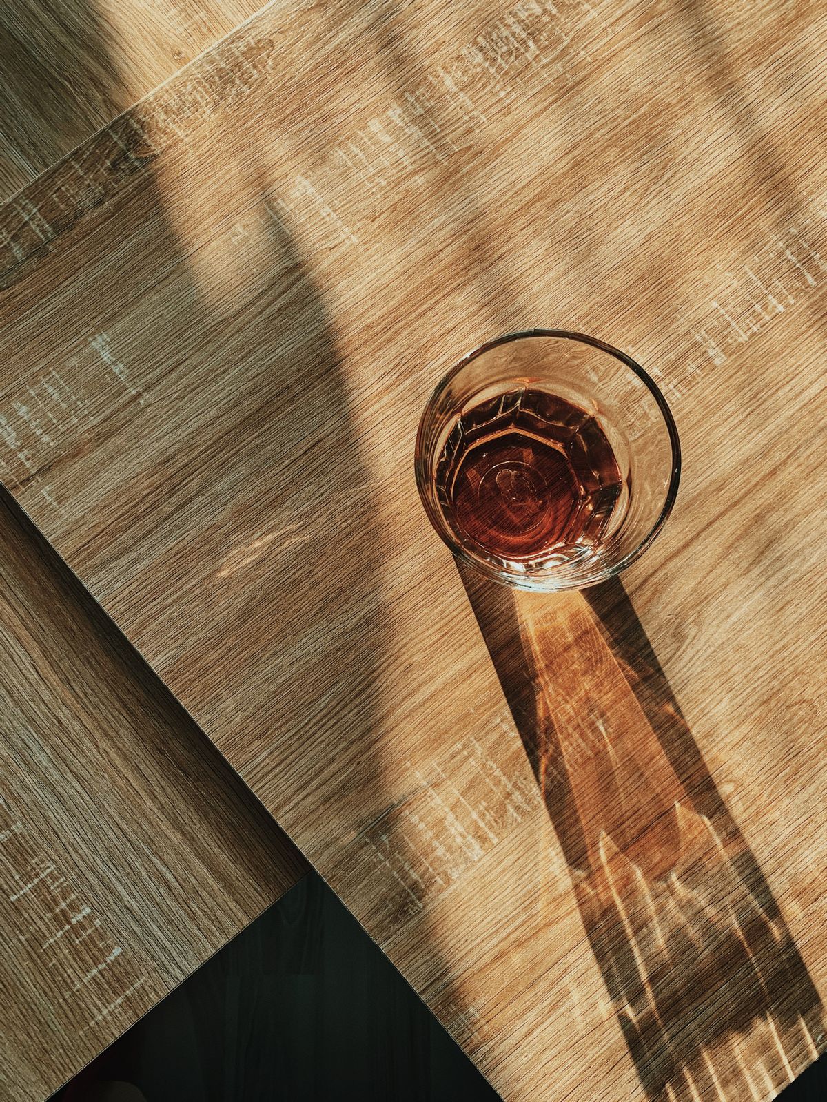 Glass of water casting a shadow on a sunlit wooden table