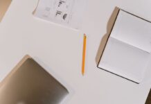 Notebook and pencil beside a laptop on a white desk