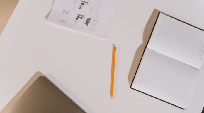 Notebook and pencil beside a laptop on a white desk