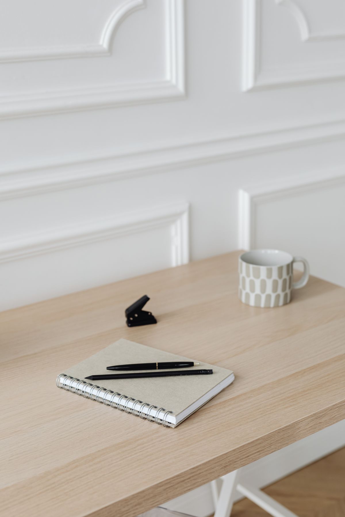 Notebook and pen beside a mug and stapler on a wooden desk