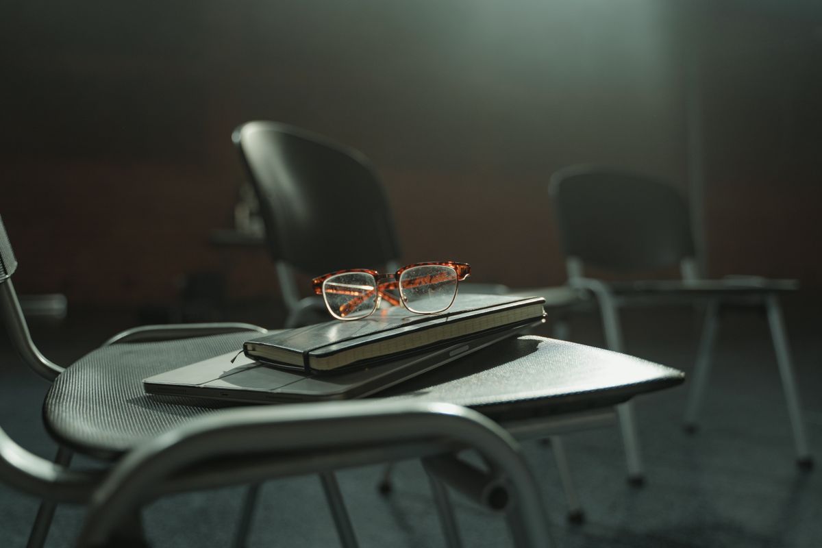 Notebook and brown-framed eyeglasses resting on a black chair in an indoor meeting space