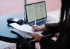 Person writing on paper at a table beside an open laptop