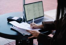 How Couples Can Make an Emergency Contact Plan Without Sharing Every Password Person writing on paper at a table beside an open laptop