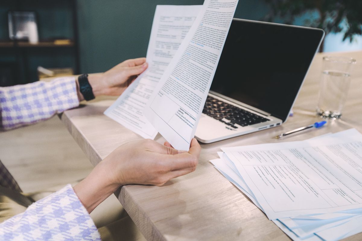 Hands reviewing printed documents beside a laptop on a desk