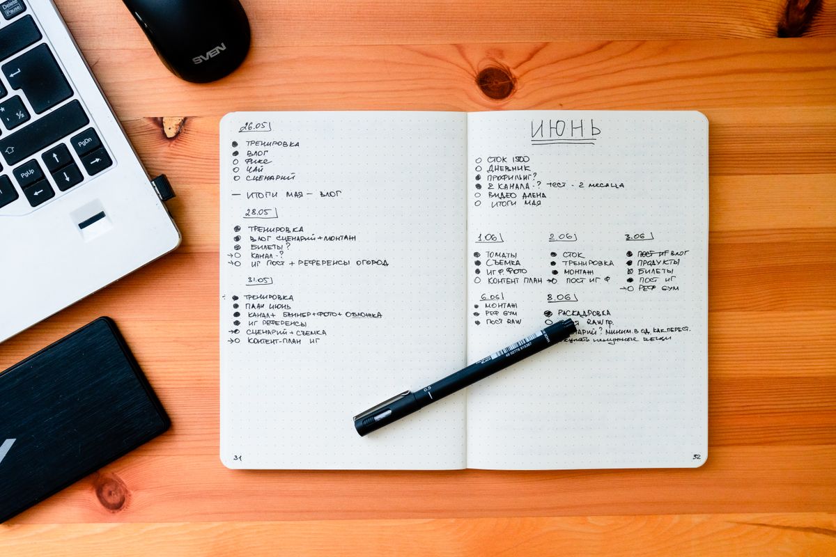 Open notebook with handwritten notes beside a laptop and pen on a wooden desk