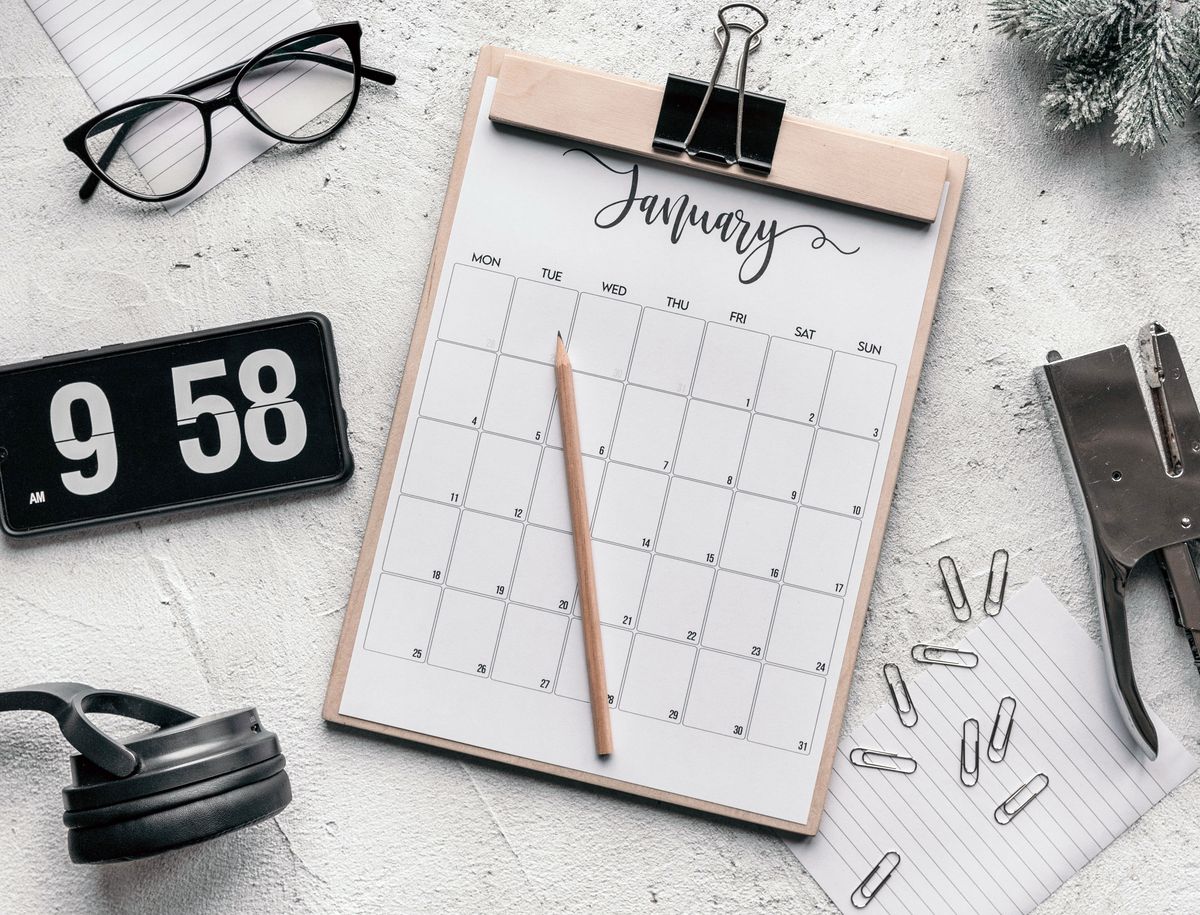 Calendar on a clipboard beside a clock and stationery on a desk