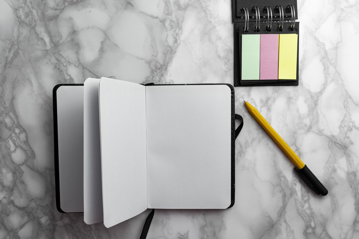 Blank notebook with a pen and colorful sticky notes on a marble surface