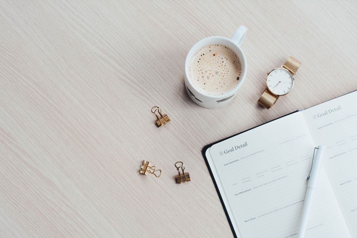 Open planner beside a coffee cup and wristwatch on a wooden surface