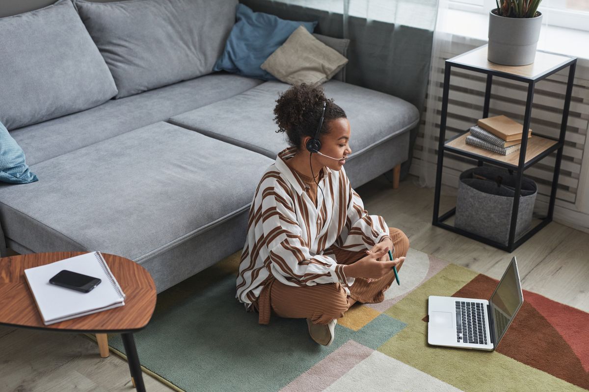 Woman sitting on the floor at home with a laptop and headset