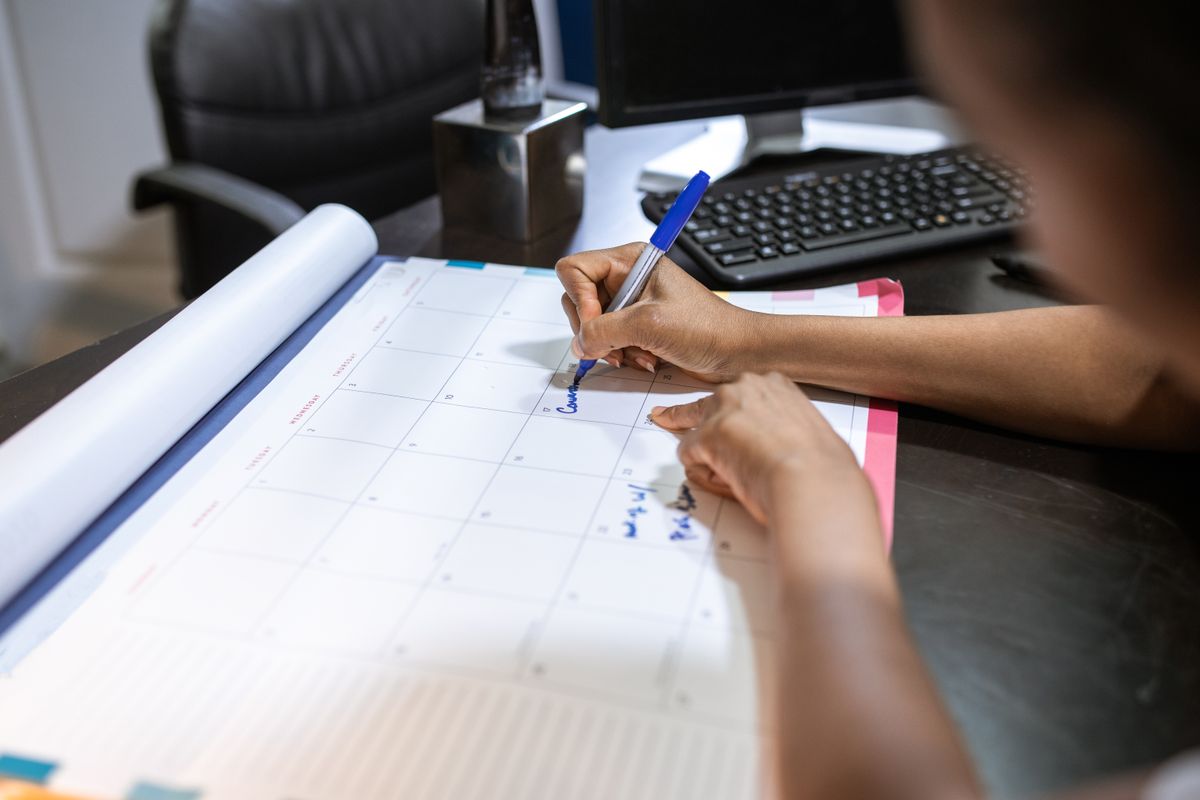 Person writing appointment notes on a desk calendar