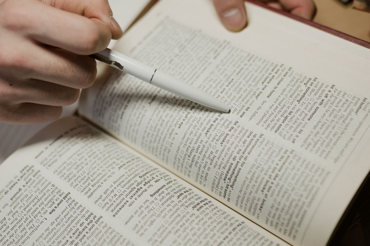 Hand pointing a pen at text in an open book