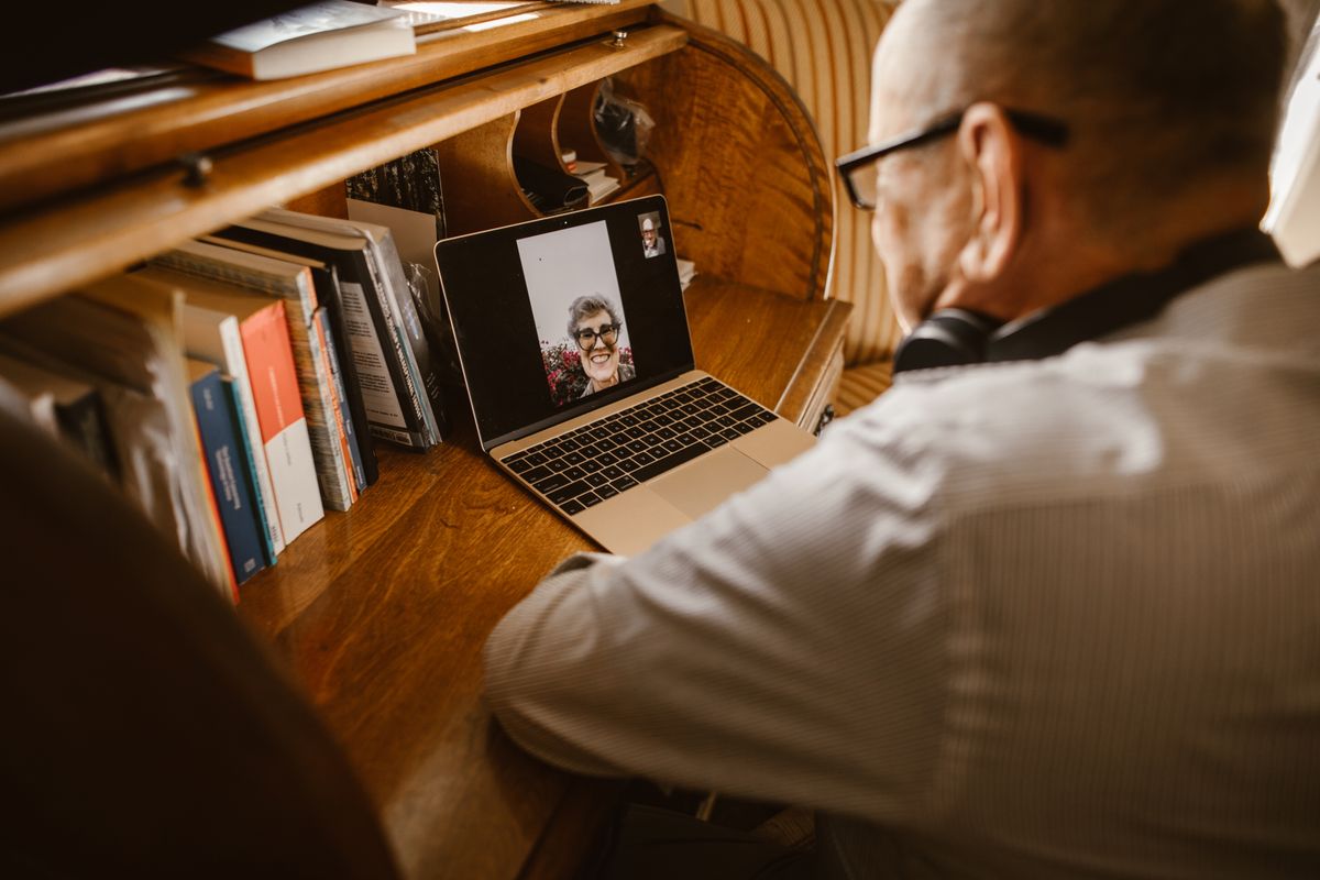 Older man at a desk speaking with a woman on a laptop video call