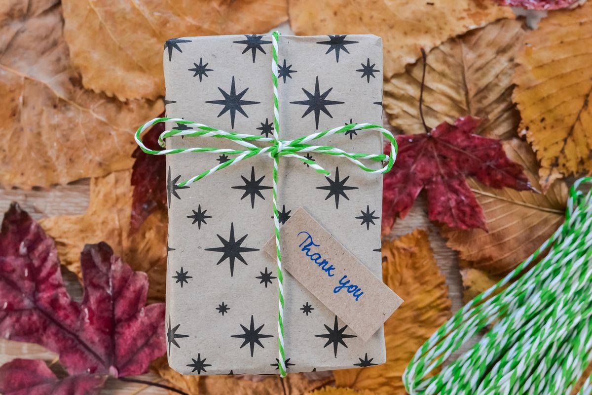 Wrapped gift box with a thank you note resting on autumn leaves