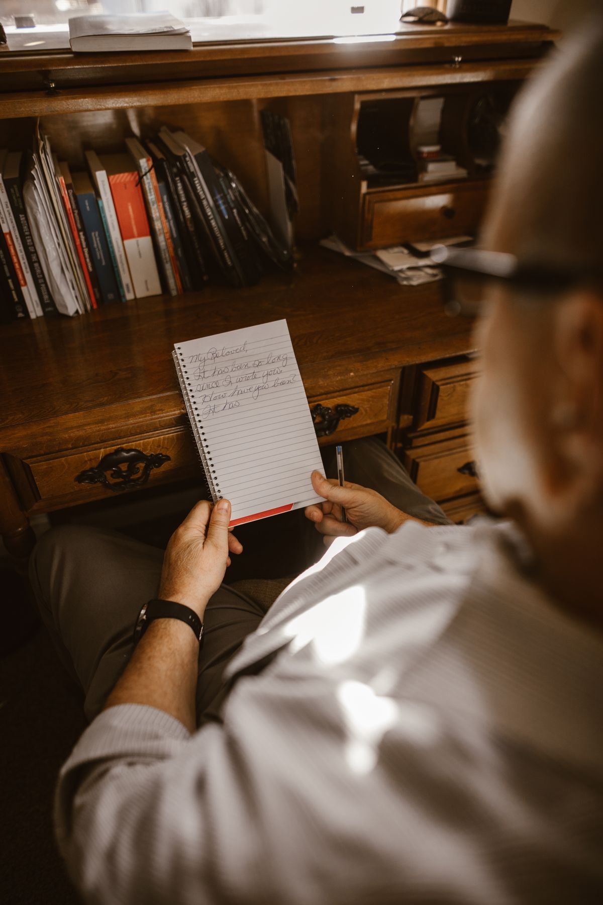 Hand holding a spiral notebook with handwritten notes at a wooden desk