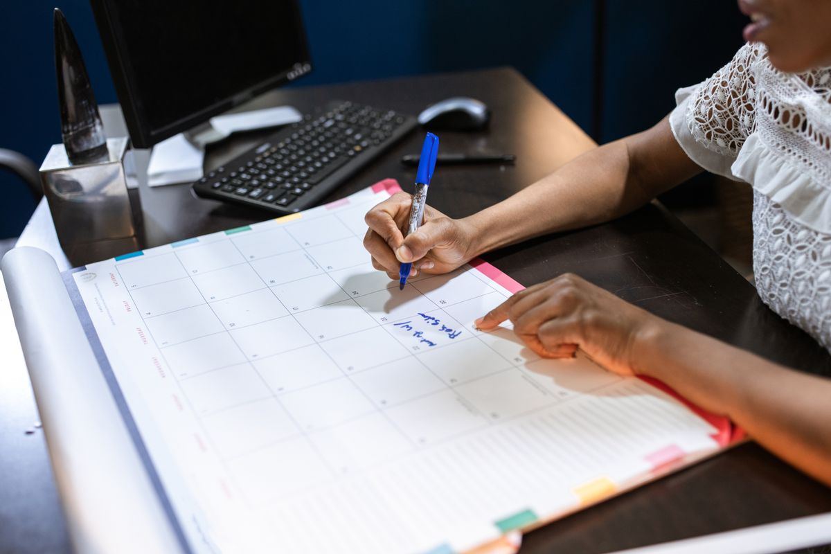 Hand holding a pen while adding notes to a desk calendar
